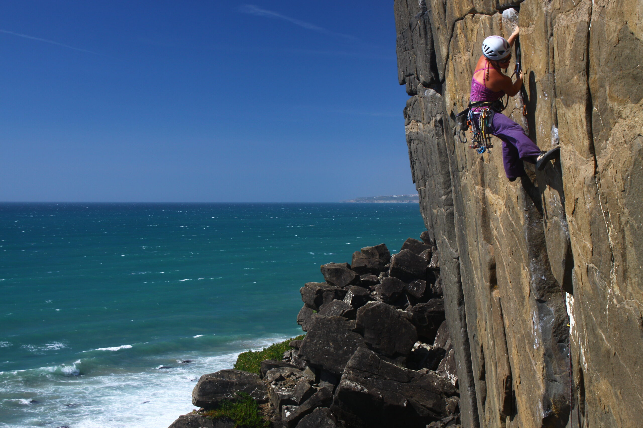 Inma Garrido aparece a la derecha de la foto escalando en una pared vertical. Al pie de vía se ven rocas y el mar que también ocupa toda la parte izquierda de la foto. Está tomada en Portugal en Casal de Pianos y el crédito de la foto es de Iván Jara.