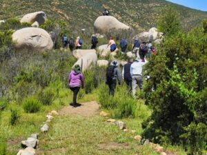 Grupo de senderistas aparece caminando de espaldas hacia unas grandes piedras redondeadas