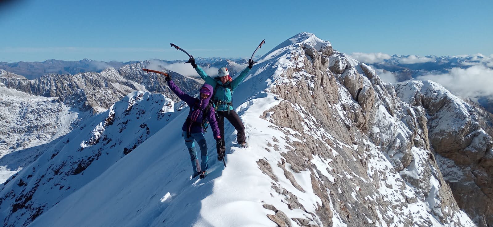 Mujeres celebrando el estar en la cima de una montaña nevada.
