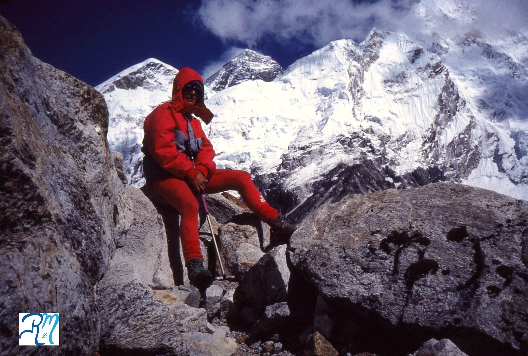 Reyes aparece sentada en unas grandes rocas con ropa de alta montaña roja, cubierta cabeza con capucha y gafas de nieve. Tras ella tres de las grandes montañas del Himalaya: Everest, Nuptse y Lhotse.